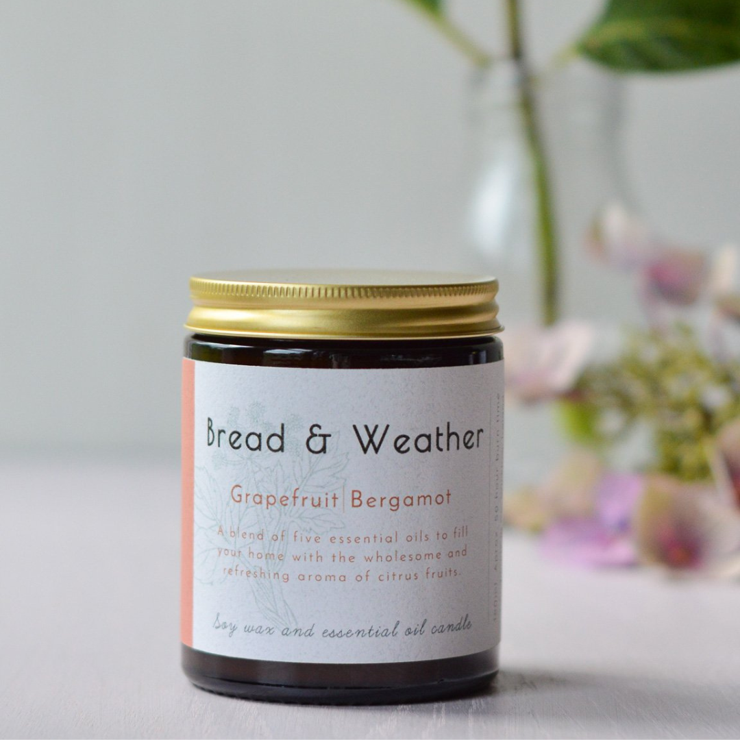 A picture of a candle in a jar with a cold lid and flowers in the background 