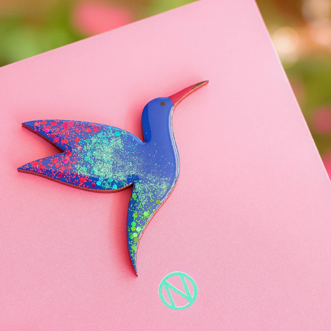 A blue hummindbird brooch with red and green speckles